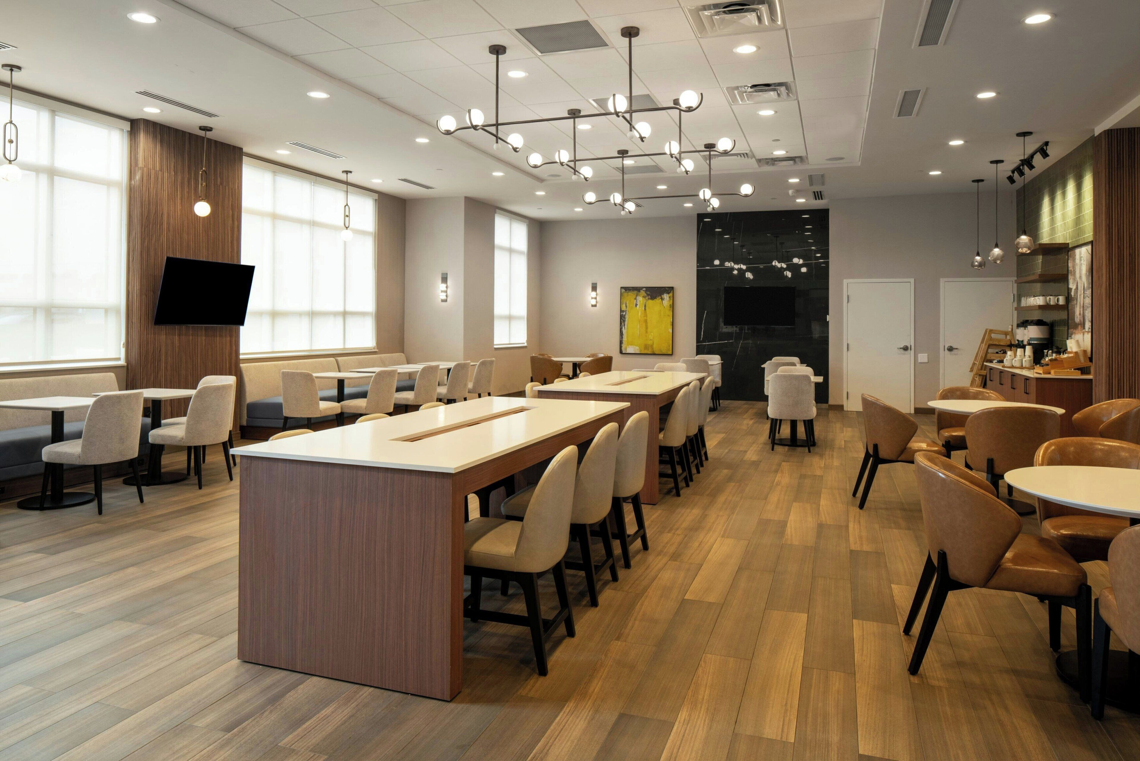 A modern dining area with multiple tables and chairs, a central island, and a flat-screen TV mounted on the wall.