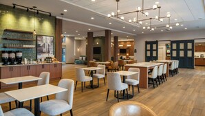 A modern restaurant with wooden flooring, multiple dining tables and chairs, a bar area, and a large TV screen. - Residence Inn By Marriott Montgomery Downtown (Montgomery)