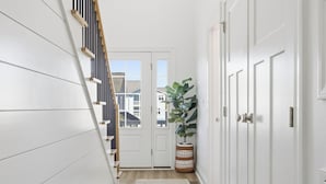A hallway with white walls, a wooden staircase, a large potted plant, and a door leading to a balcony. - Surf street + Near the Beach + Pet friendly (North Myrtle Beach)