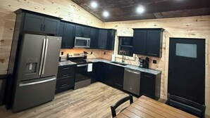 A compact kitchen with wooden walls, a refrigerator, microwave, sink, and a dining table. - New Cozy Country barndominium located in Leitchfield, KY. (Leitchfield)