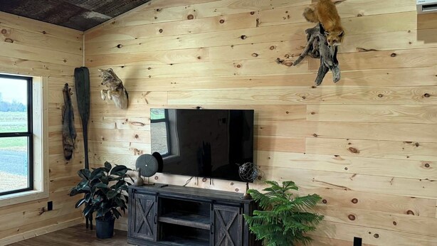 A rustic interior with wooden walls, a mounted television, and various wall-mounted animal heads. - New Cozy Country barndominium located in Leitchfield, KY. (Leitchfield)