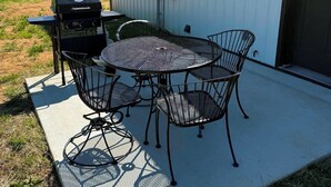 A patio with a round table and chairs, a grill, and a building with windows and a door. - New Cozy Country barndominium located in Leitchfield, KY. (Leitchfield)