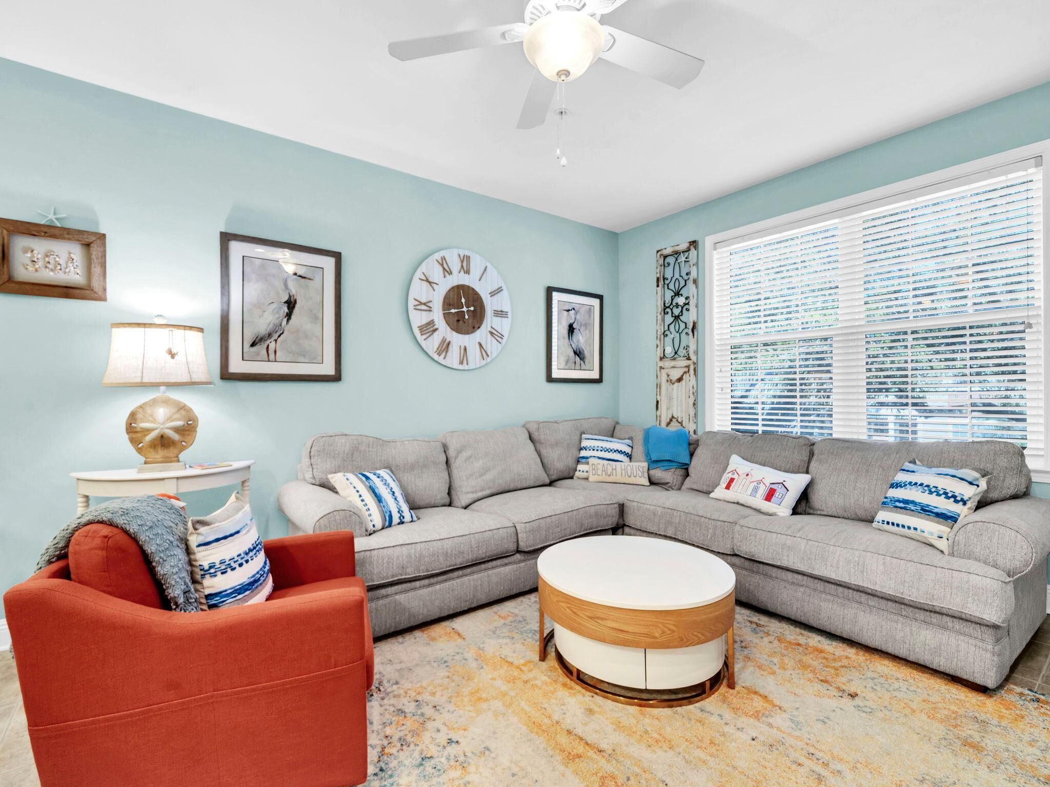 A living room with a grey sectional sofa, a red armchair, a round coffee table, and a ceiling fan.