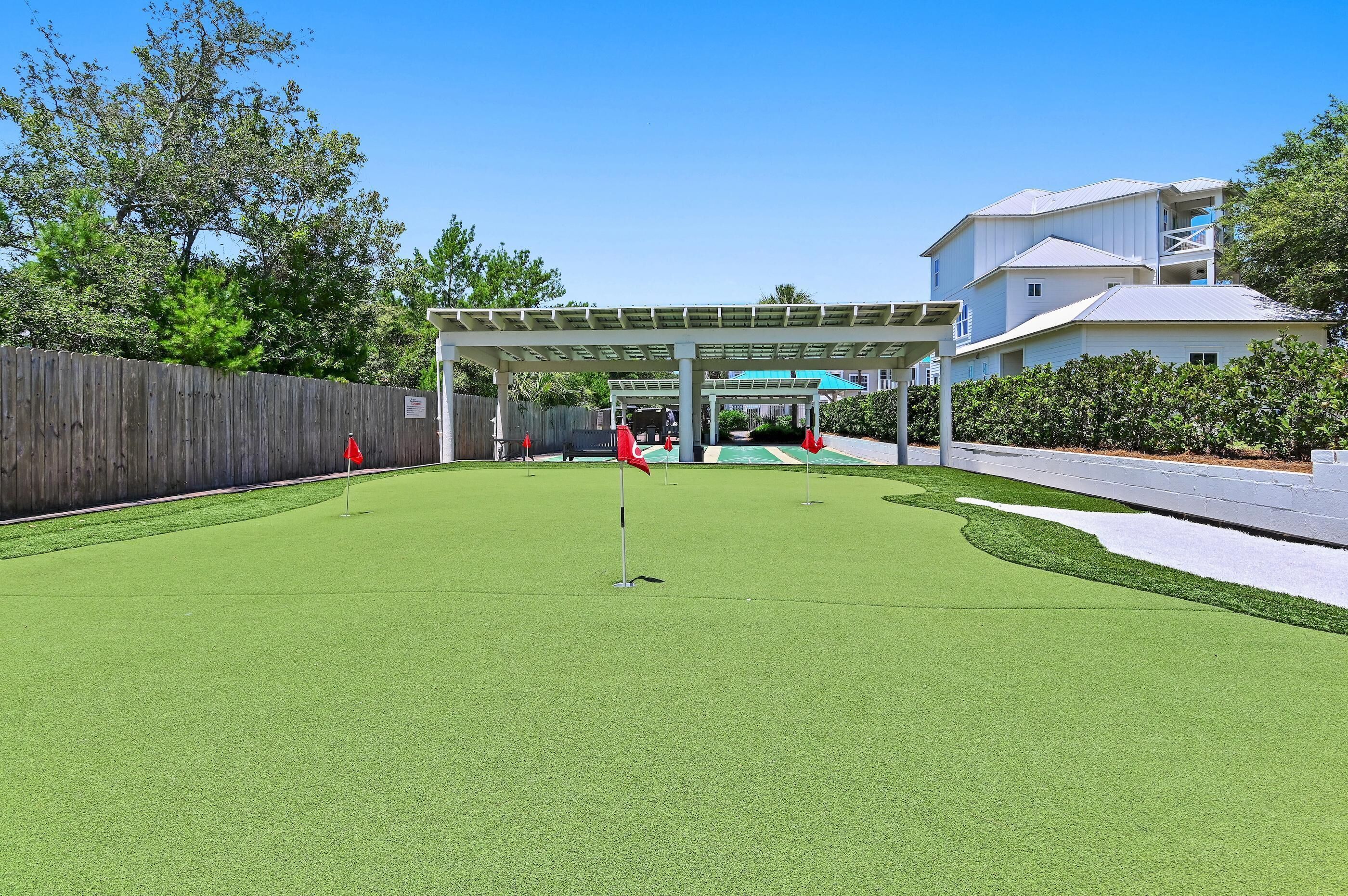 A golf course with a covered pavilion, a wooden fence, and a building with a balcony.