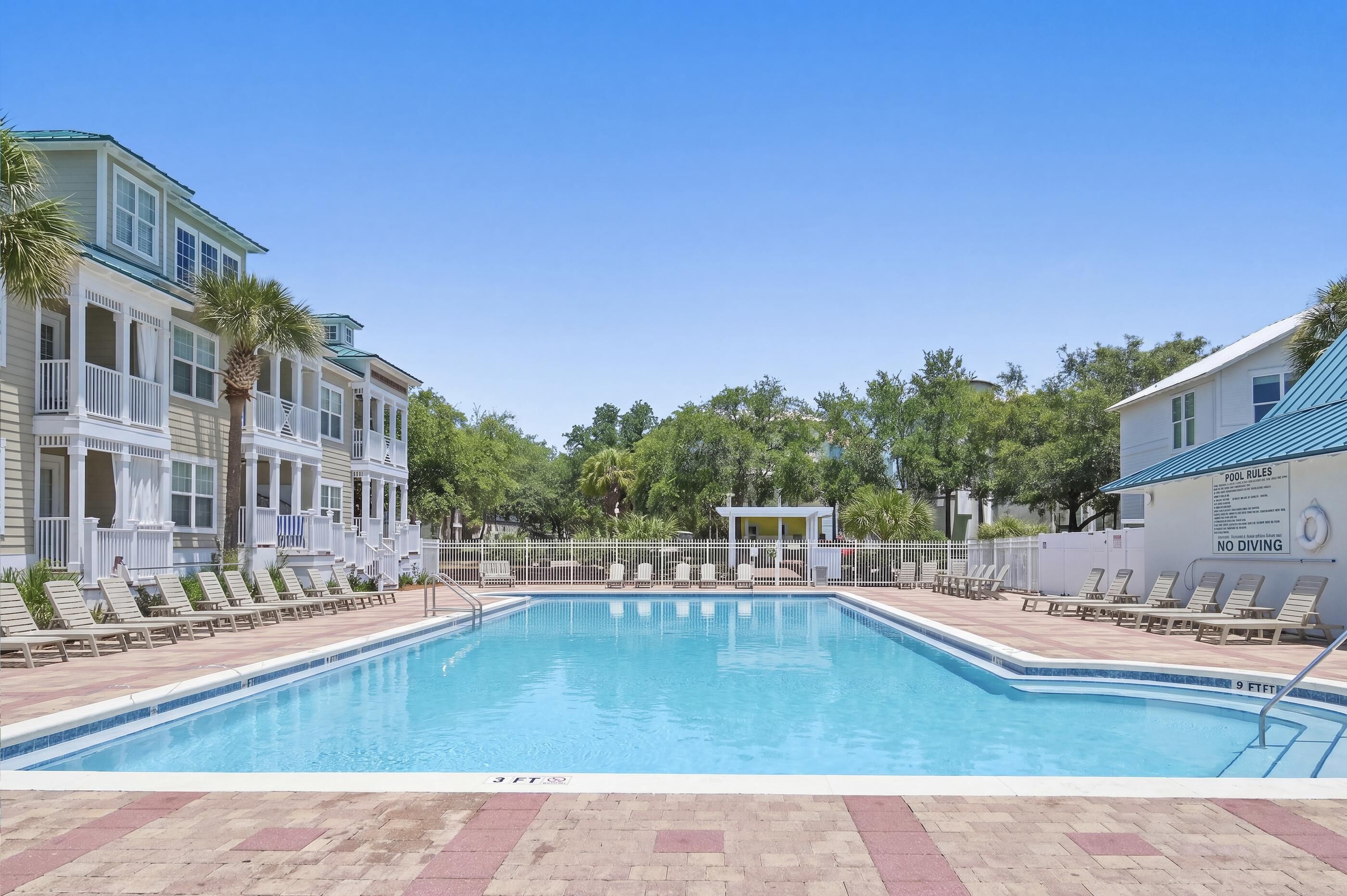 A swimming pool with lounge chairs, a pool rule sign, and a building with balconies.