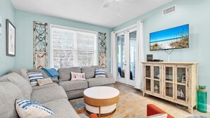 A living room with a grey sectional sofa, a round coffee table, a wooden cabinet, and a beach-themed painting on the wall. - The Village 622 (Santa Rosa Beach)