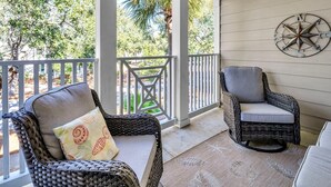 A covered porch with wicker furniture and a decorative compass wall piece. - The Village 622 (Santa Rosa Beach)