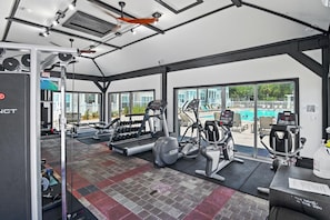 Ein Fitnessraum mit Trainingsgeräten, einem Laufband und Blick auf einen Pool.