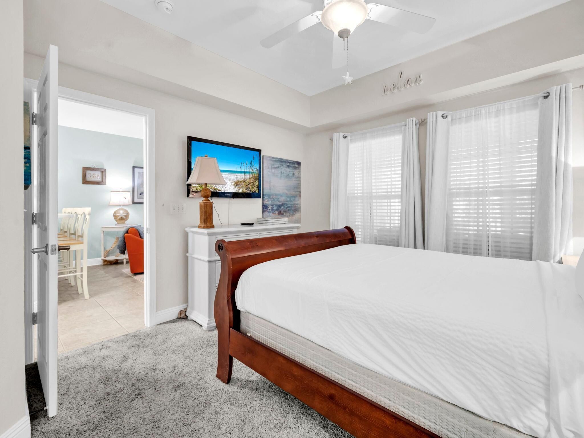 Un dormitorio con cama, escritorio, silla, televisor y ventana con cortinas.