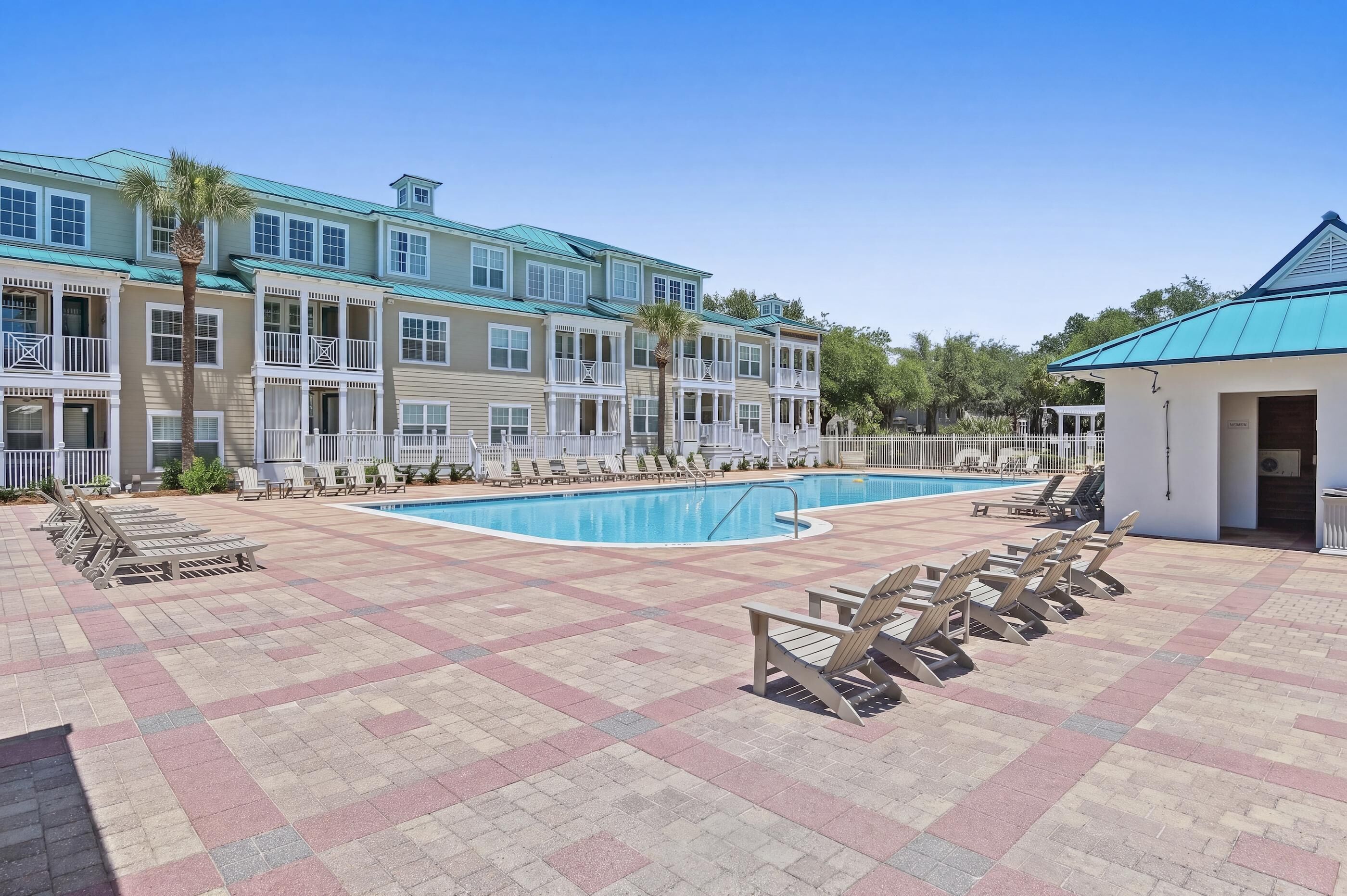 Un área de piscina con sillones reclinables, un edificio con techo azul y una palmera.