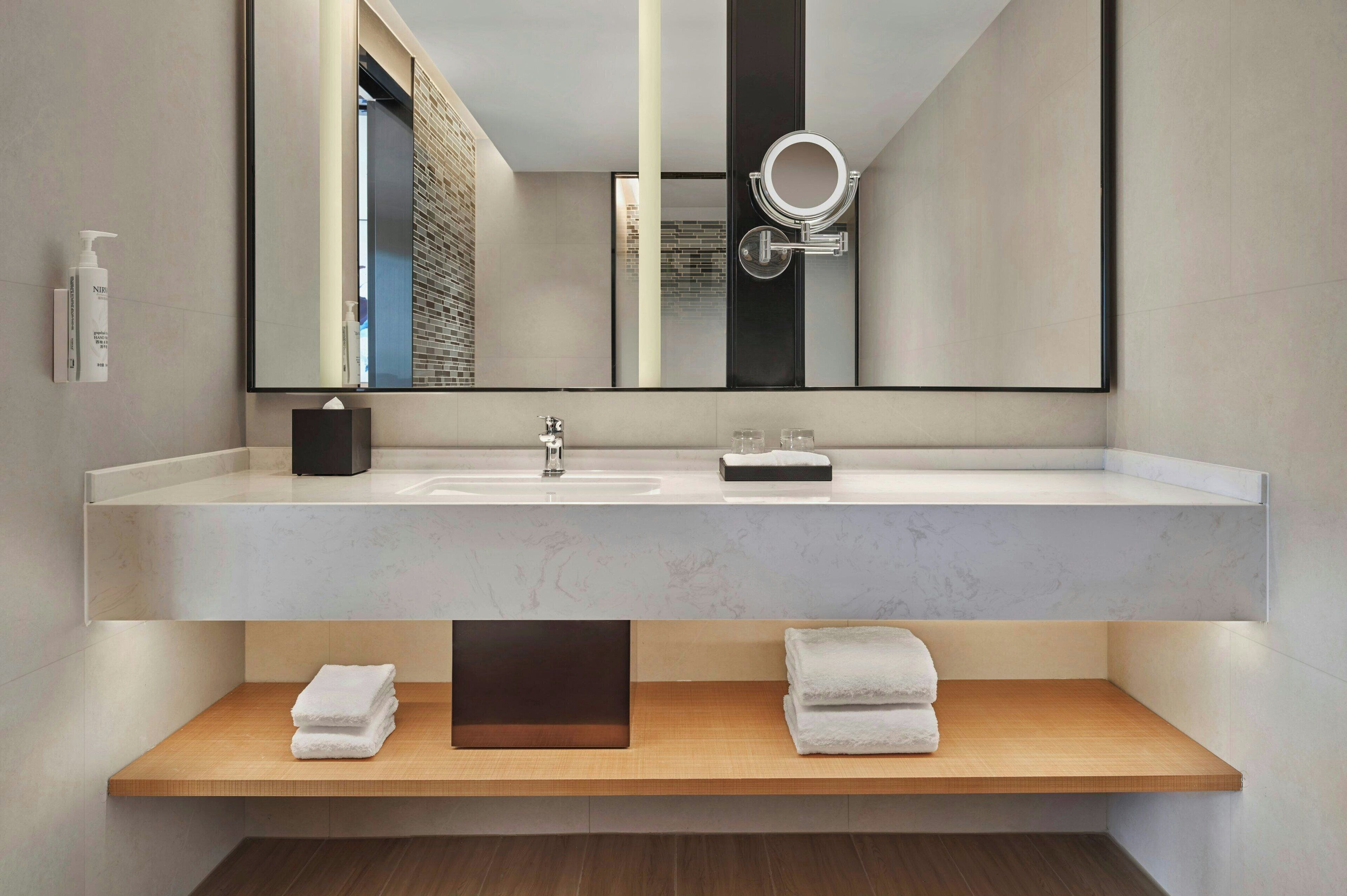 A modern bathroom with a large mirror, a white sink, and two wooden shelves with towels.