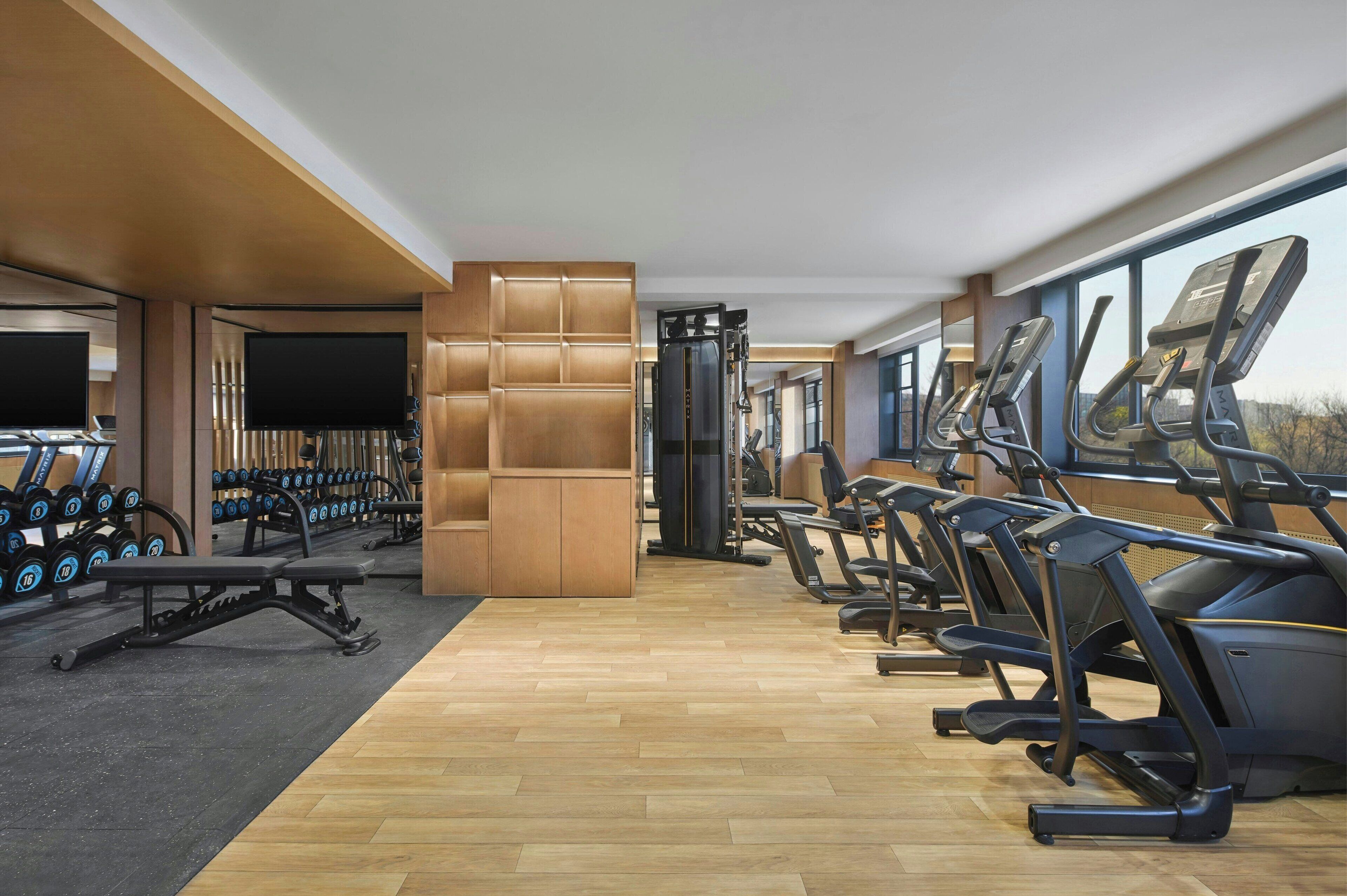 Un gimnasio con cintas de correr, mancuernas y una pantalla de televisión.