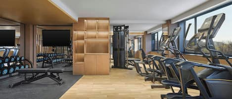 A gym with treadmills, dumbbells, and a TV screen.
