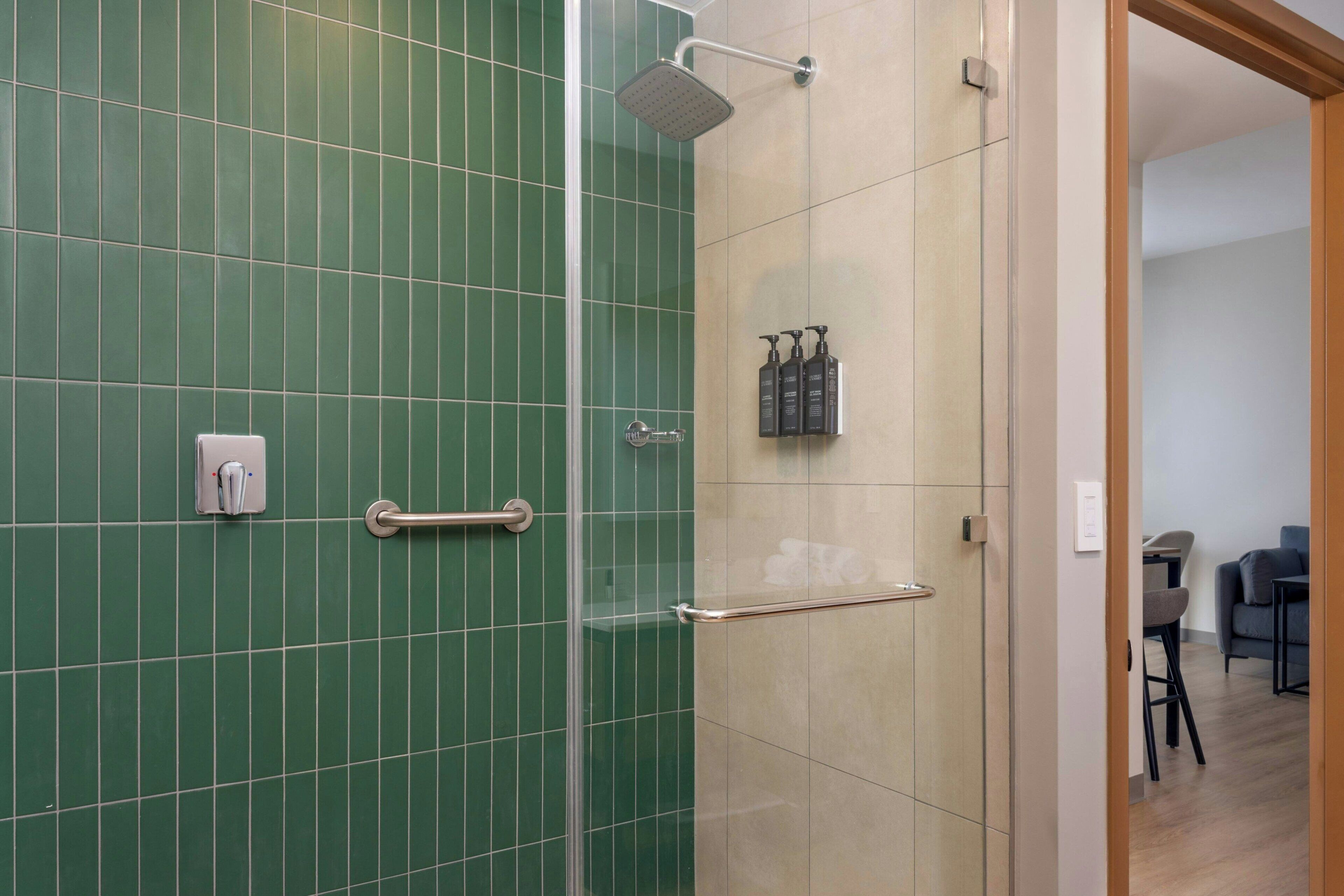 A modern bathroom with green tiles, a glass shower enclosure, and a visible toilet paper dispenser.