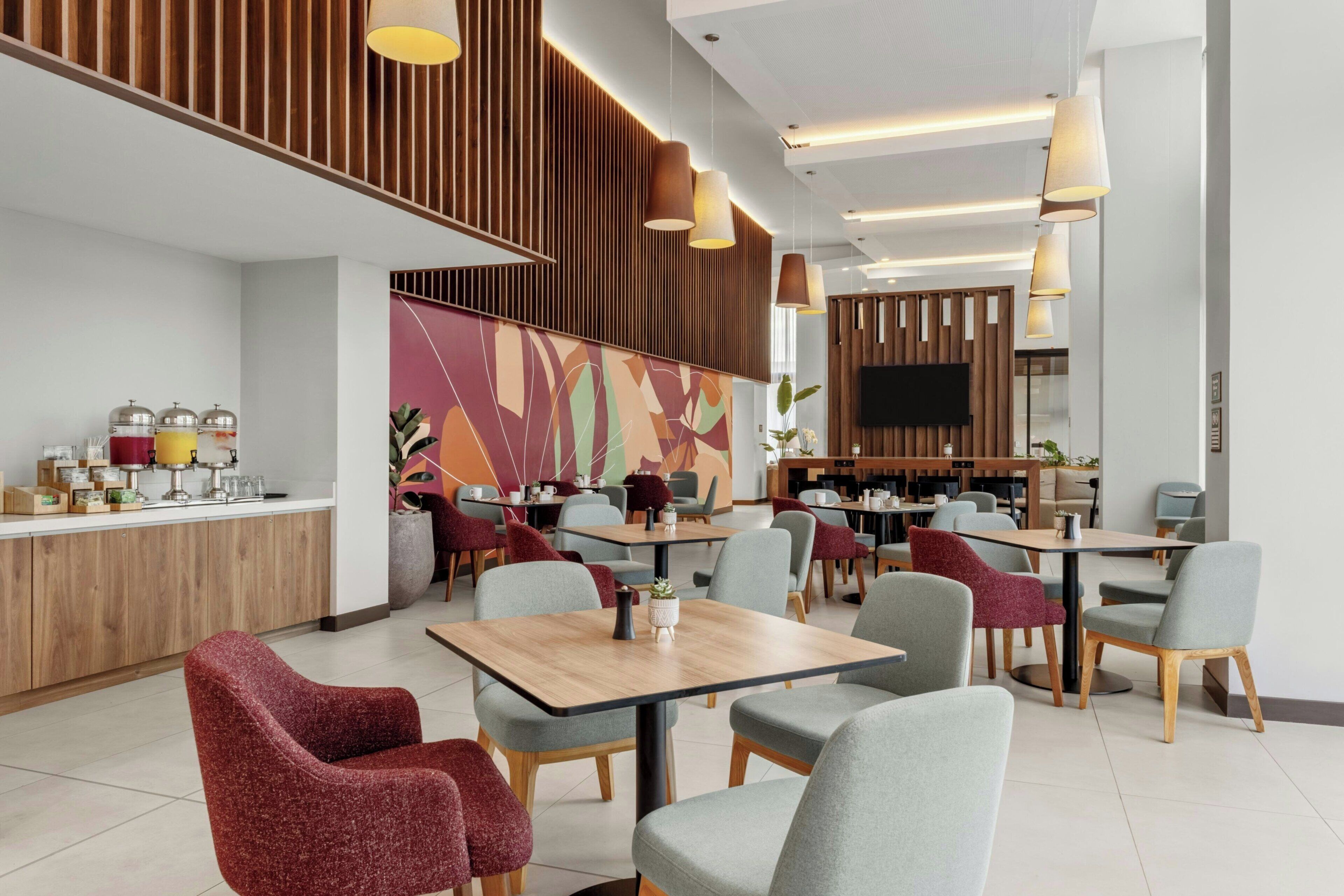 Un café moderne avec des éléments décoratifs en bois, plusieurs espaces pour s’asseoir et un téléviseur à écran plat fixé au mur.