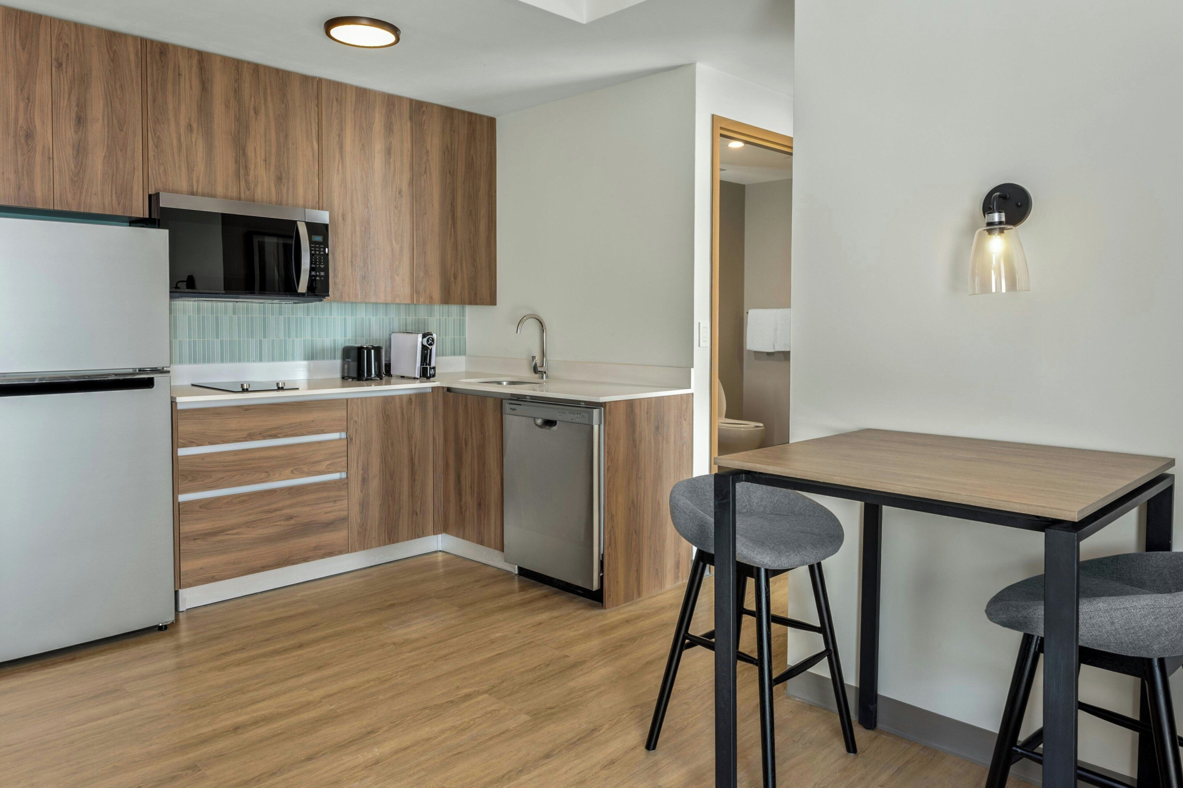 A modern kitchen with wooden cabinets, a microwave, a dishwasher, and a bar area with stools.