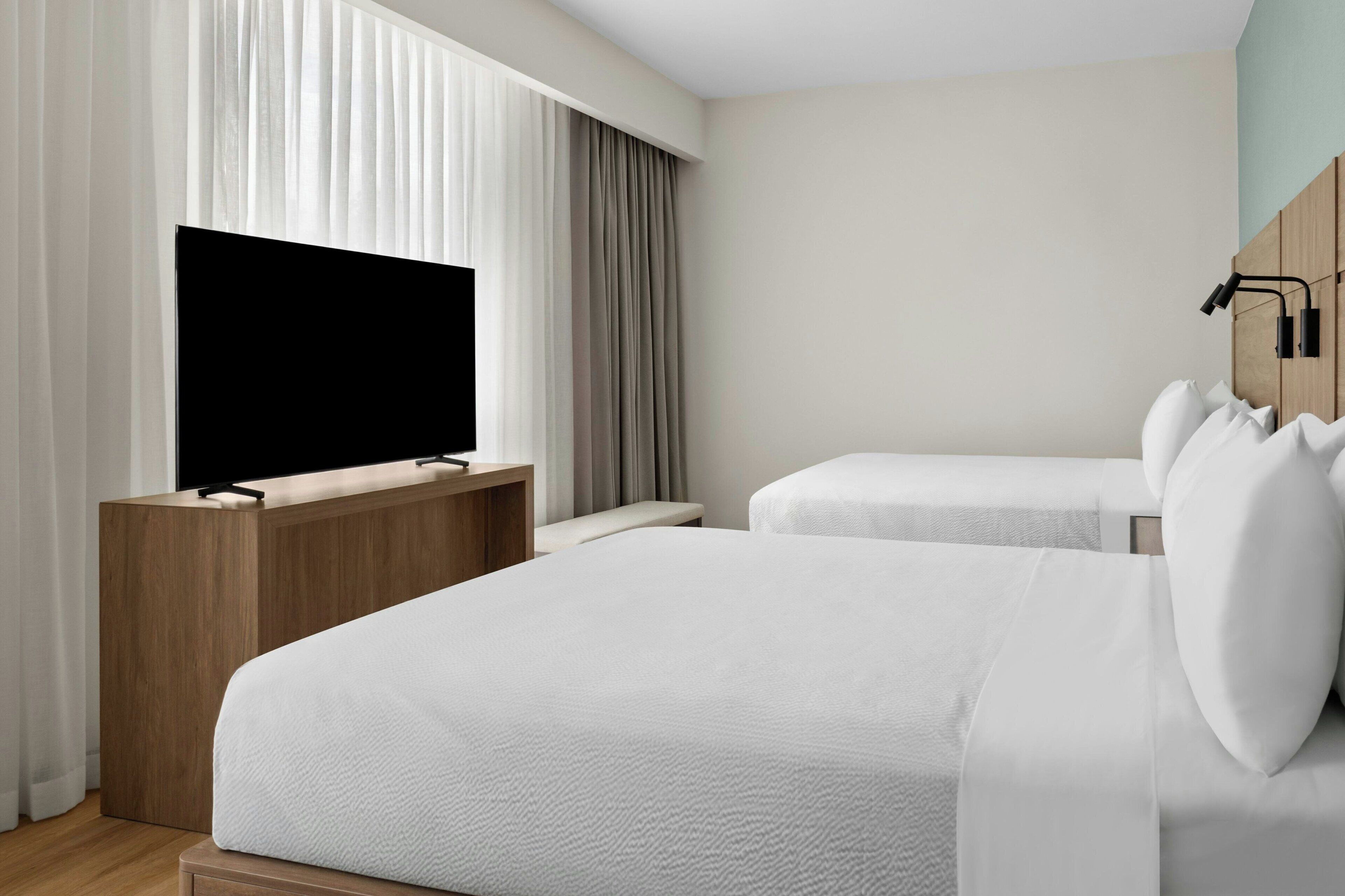 Una camera d'albergo con un letto, una televisione, una scrivania in legno e una finestra con tende.