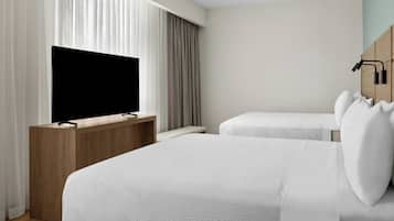 Una camera d'albergo con un letto, una televisione, una scrivania in legno e una finestra con tende.
