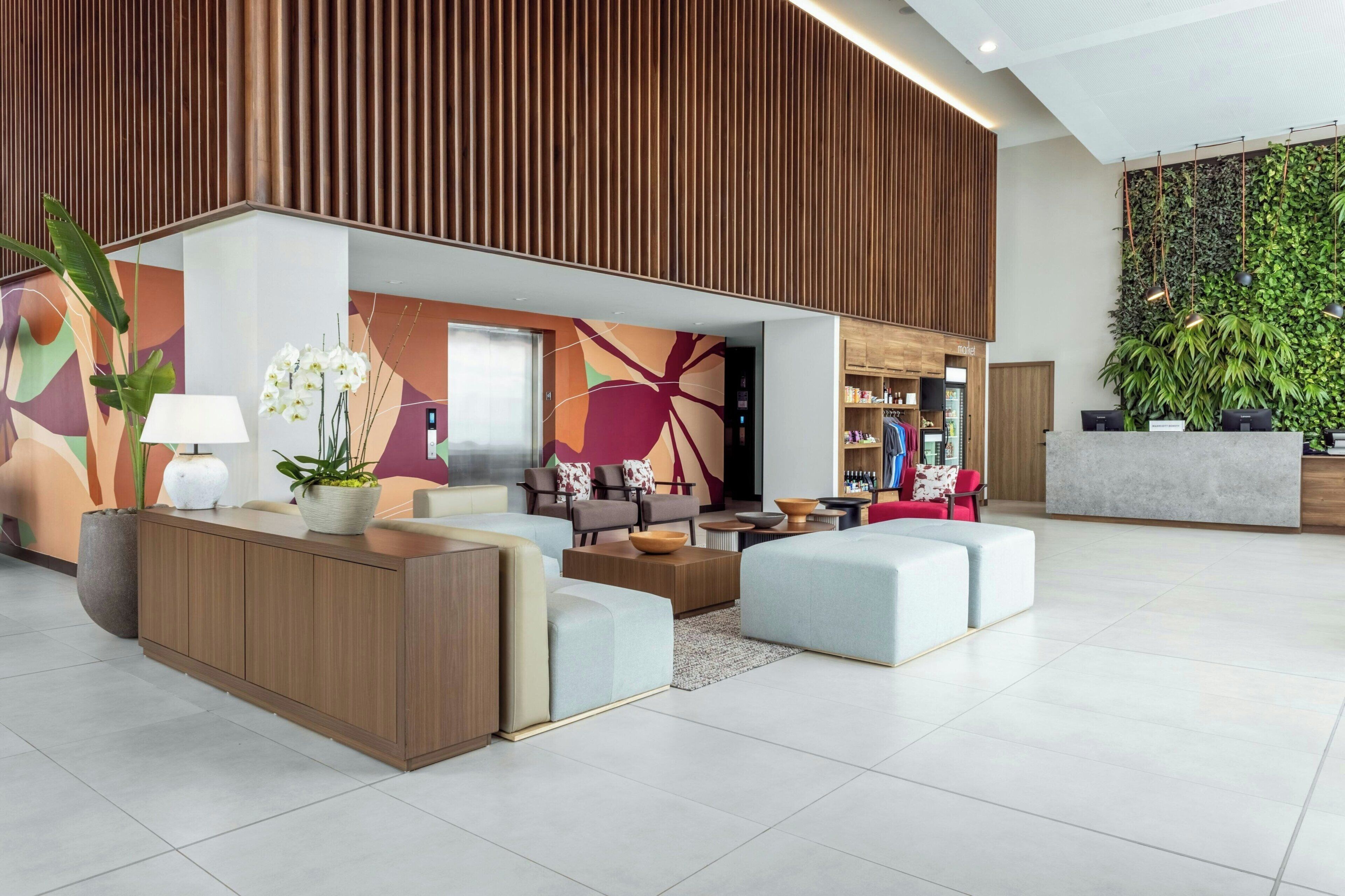 Um lobby moderno com balcão de recepção, área de estar e uma parede com ripas verticais de madeira.