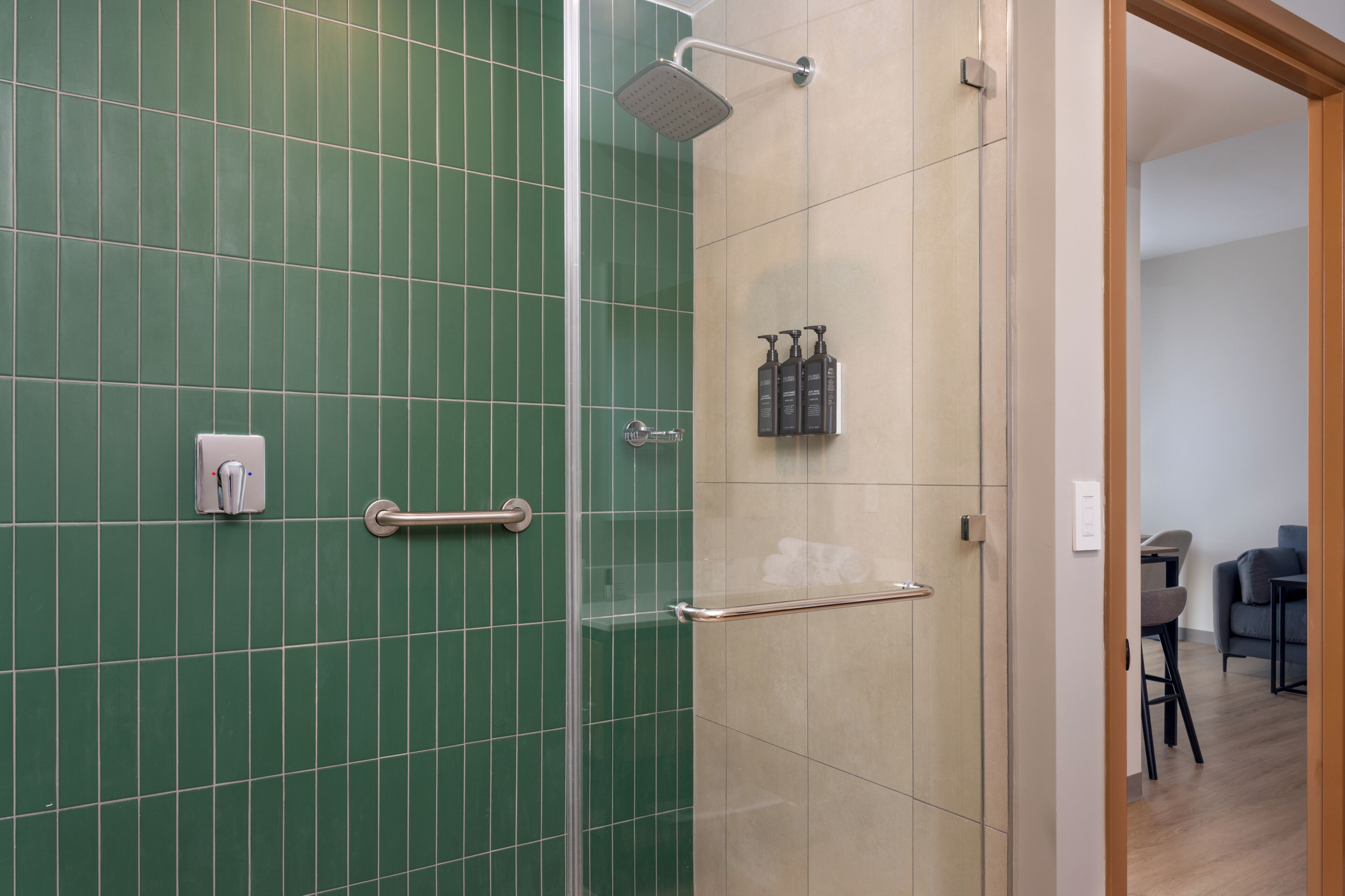 A modern bathroom with green tiles, a glass shower enclosure, and a wooden door leading to a living area.