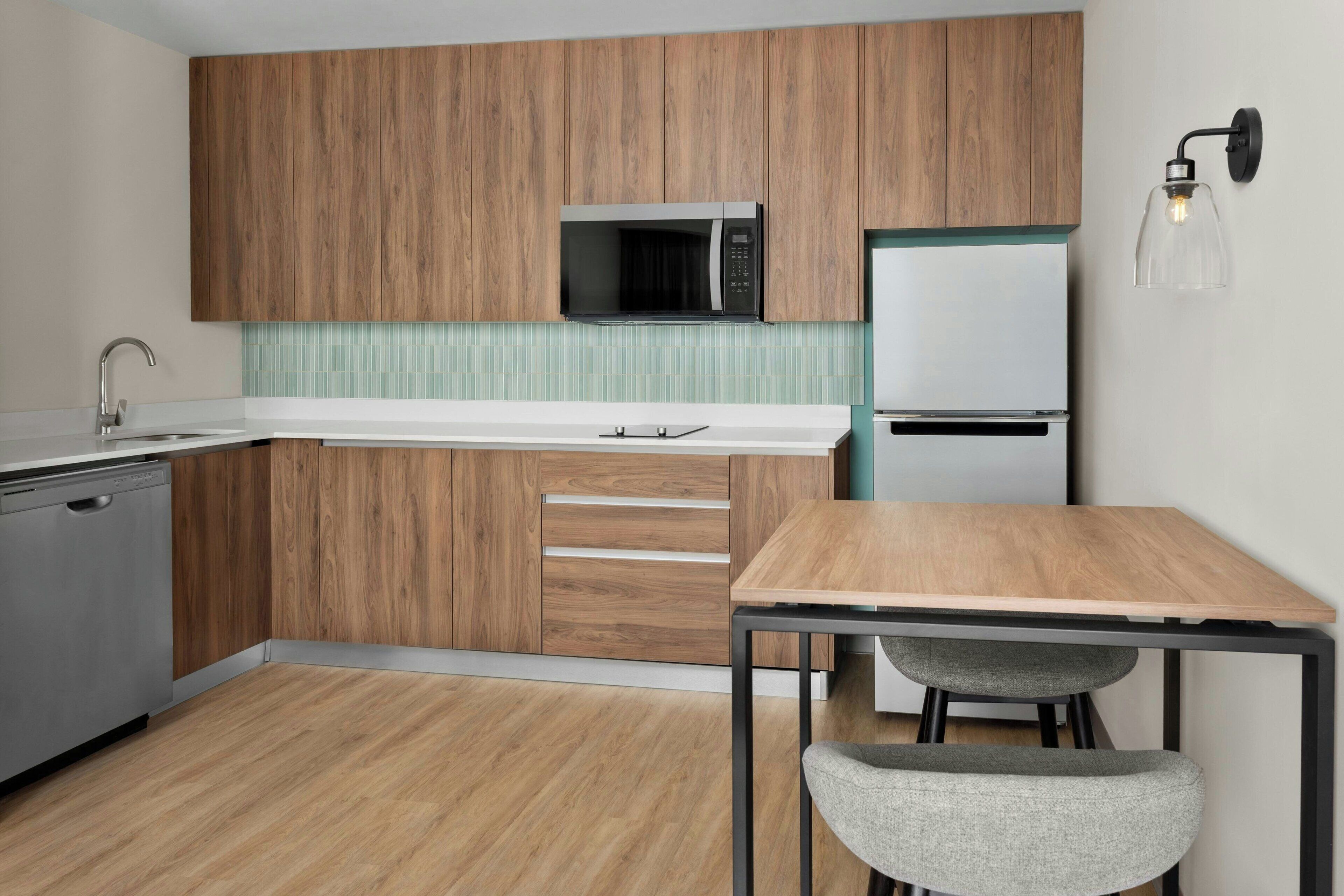 Una cocina compacta con armarios de madera, un microondas, un refrigerador, un lavavajillas, una mesa y una silla.