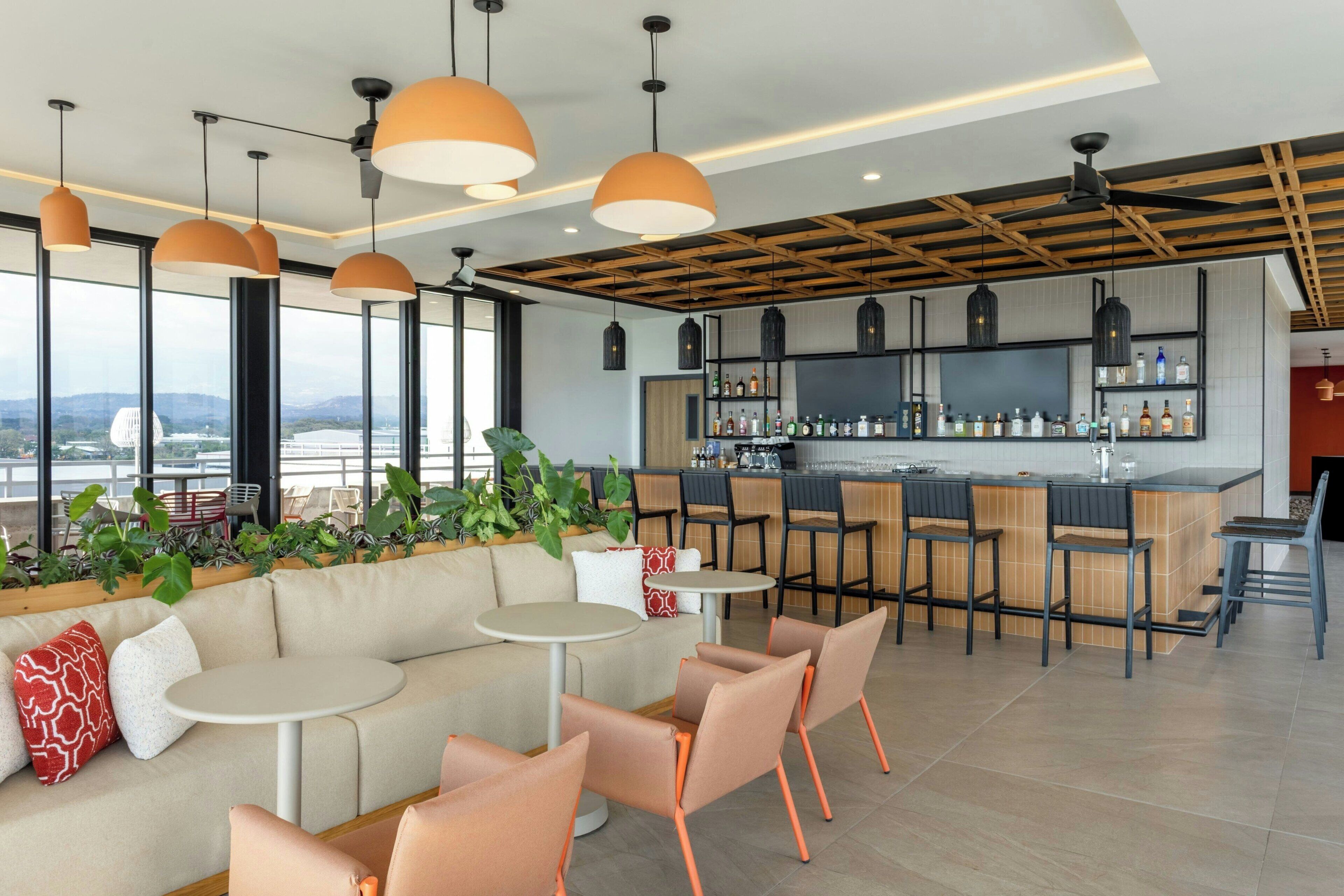 A modern bar/lounge area with seating, bar counter, and large windows.