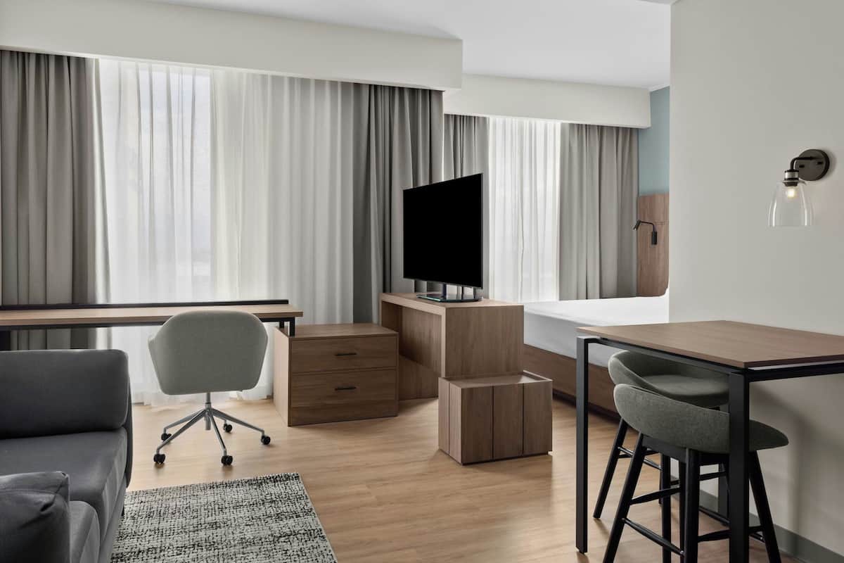 Una habitación de hotel moderna con escritorio, silla, televisor y un taburete pequeño.