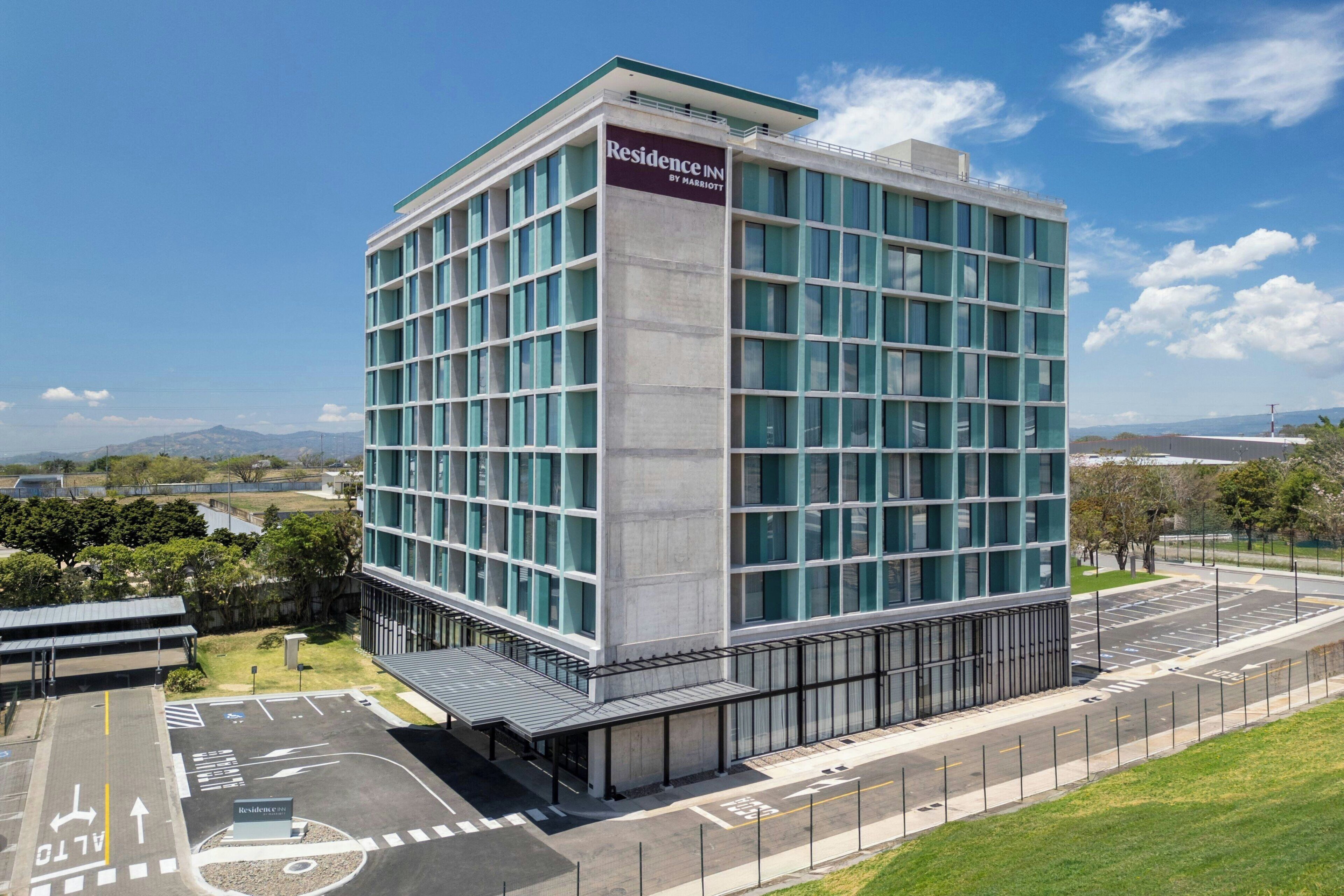 A modern building with a glass facade, a sign reading 'Residence Inn by Marriott,' and a parking lot with marked lanes.