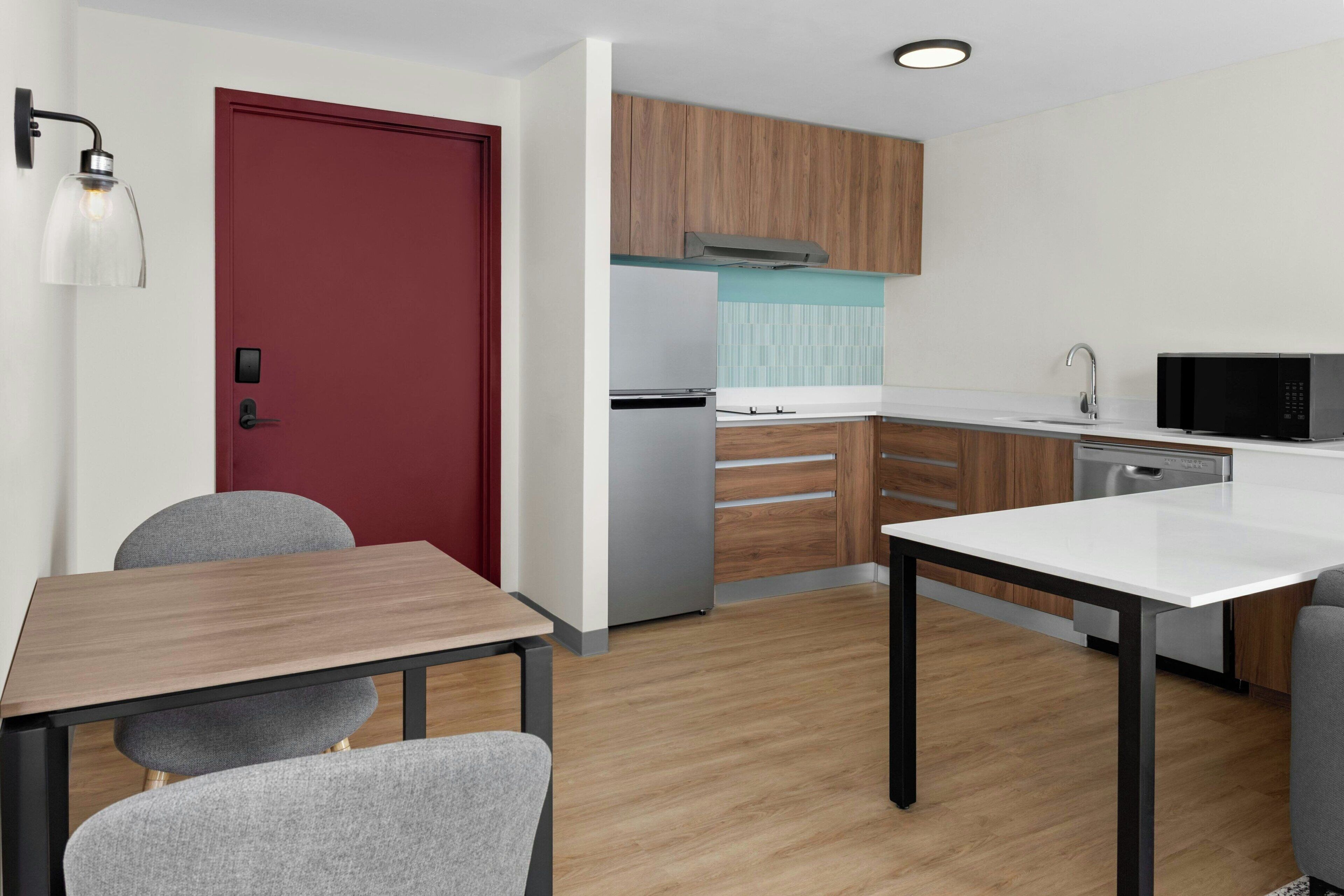 A modern kitchen with a microwave, stove, and sink. There is a dining table with chairs and a red door.