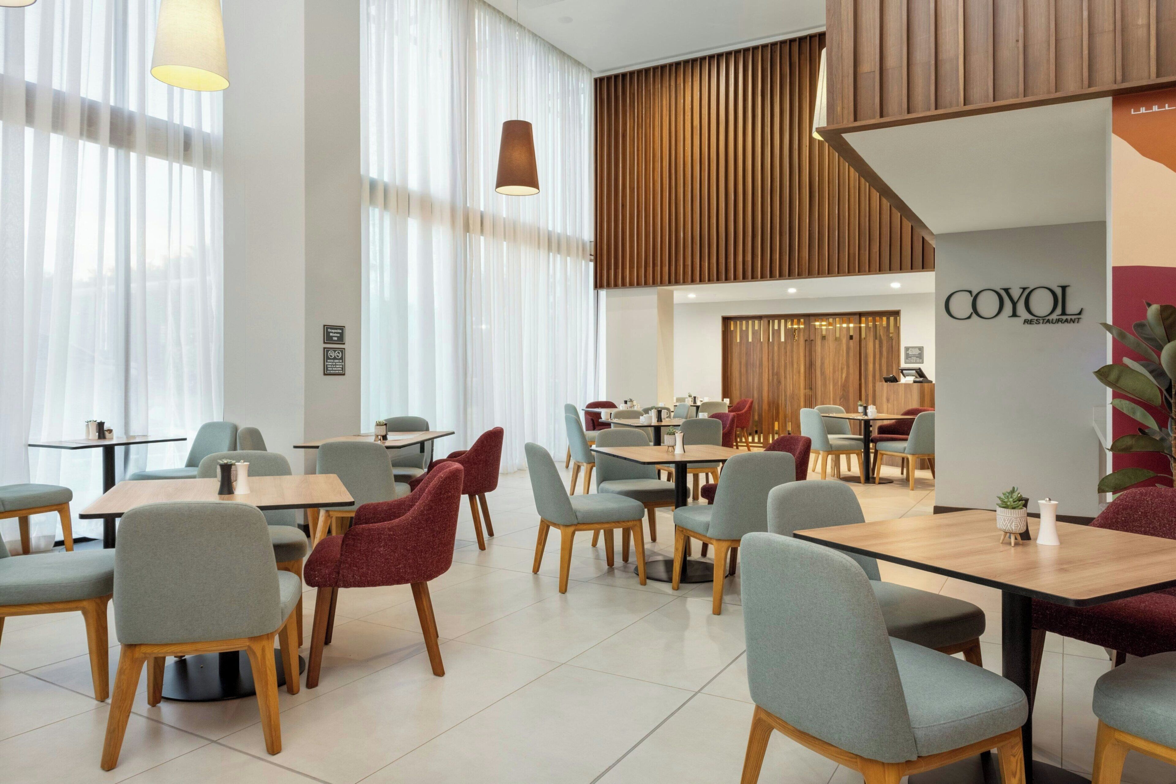 A modern restaurant interior with tables and chairs, a wooden accent wall, and a sign reading 'COYOL RESTAURANT'.