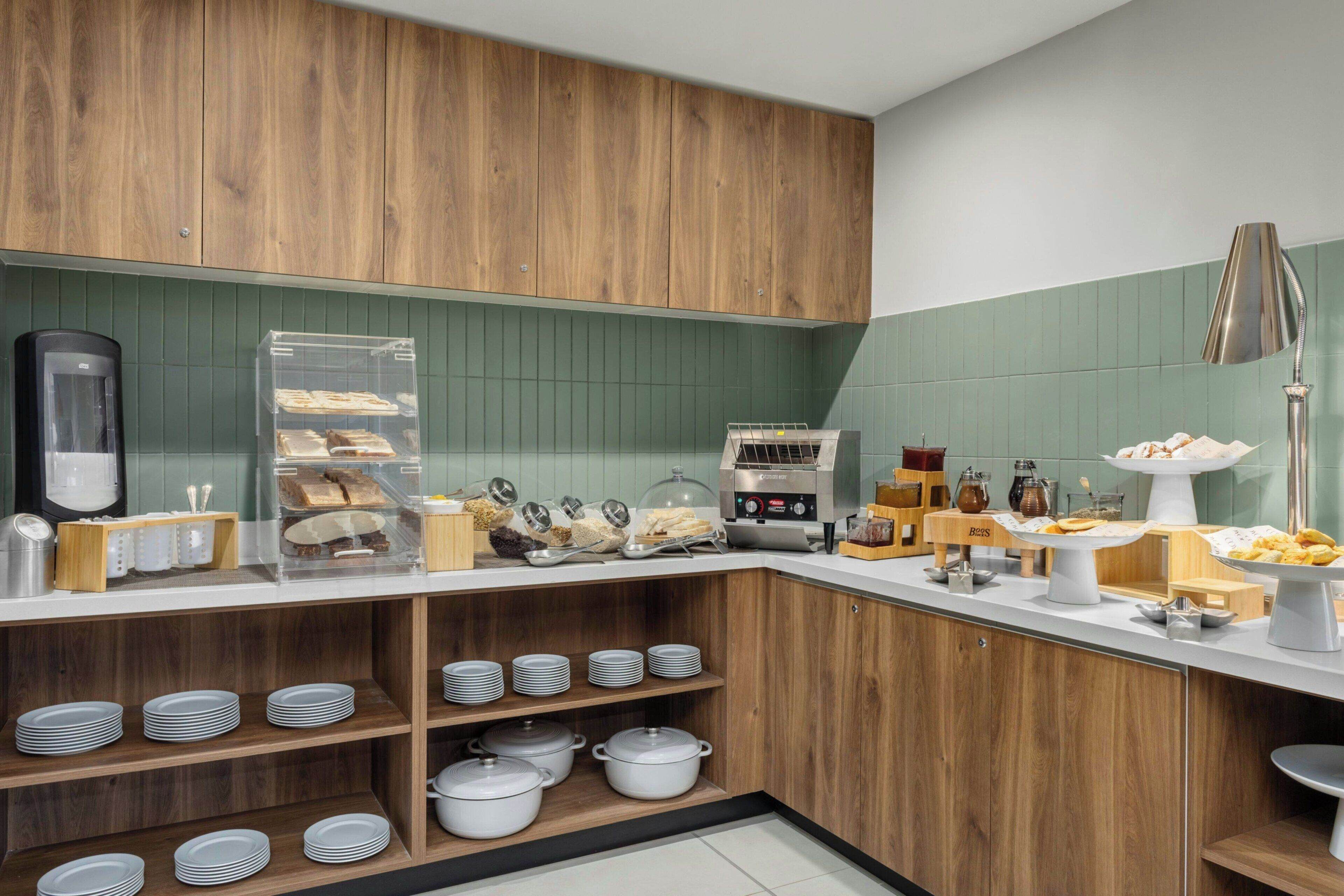 A kitchen with wooden cabinets, a coffee machine, and a buffet counter with various food items.