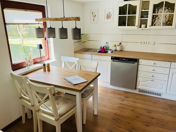 A kitchen with white cabinets, a wooden countertop, a dishwasher, and a dining area with a table and chairs. - Cozy wooden house on Fleesensee near the harbor (renovated in 2025/26) (Silz)