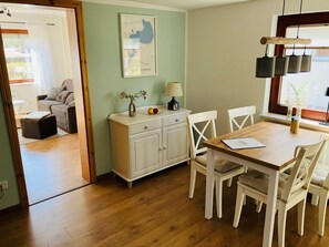 A dining area with a wooden table and white chairs, a white cabinet with a map, and a window with hanging lights.