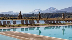 En swimmingpool med liggestole og parasoller, omgivet af skov og bjerge i baggrunden.