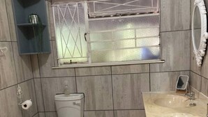 A bathroom with a toilet, a sink, a mirror, and a window with a decorative grille.