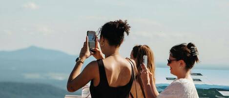 A group of people taking photos at a scenic overlook with a view of distant mountains and a body of water.