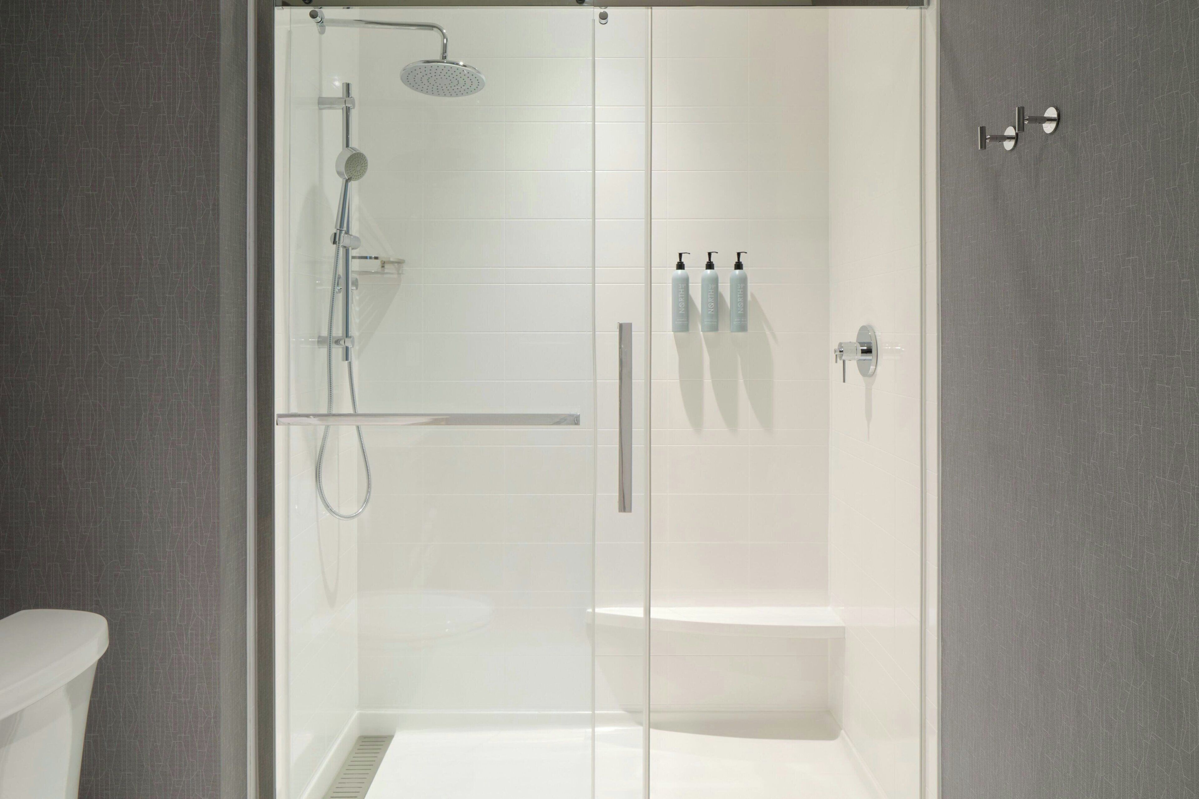 A modern bathroom with a glass-enclosed shower, a white bathtub, and a toilet.