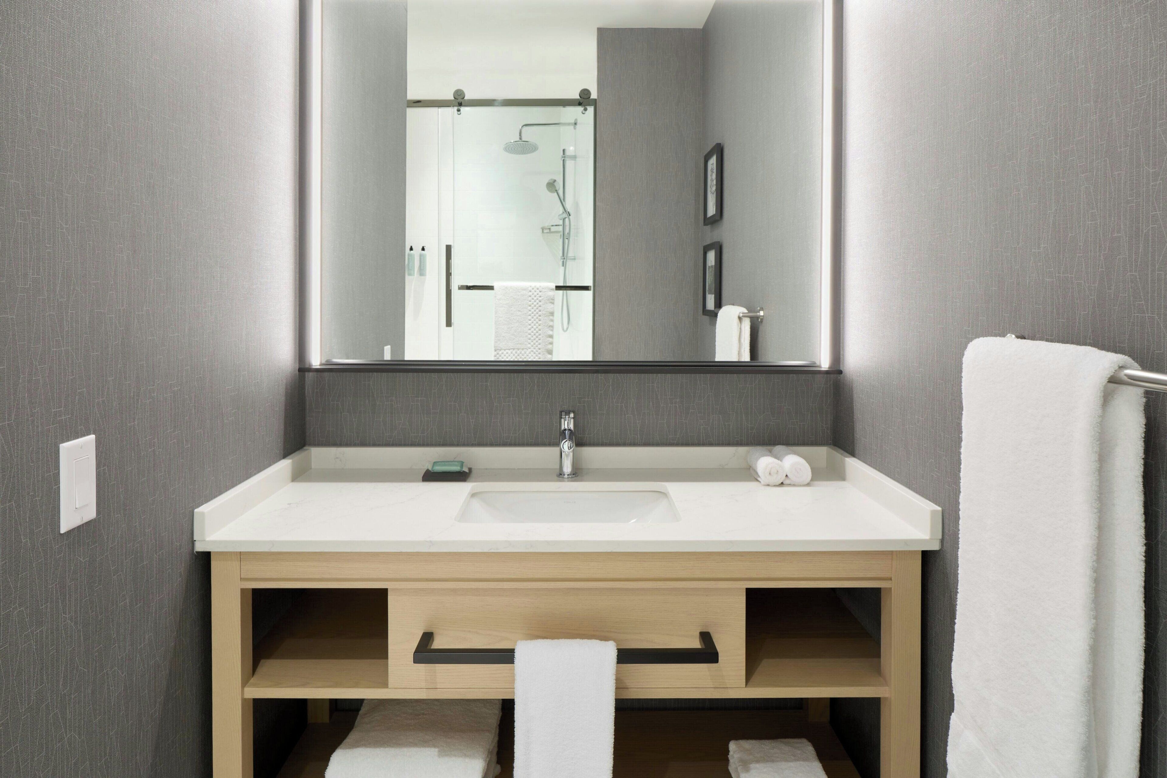 Un baño moderno con un espejo grande, un lavabo blanco y un perchero para toallas.