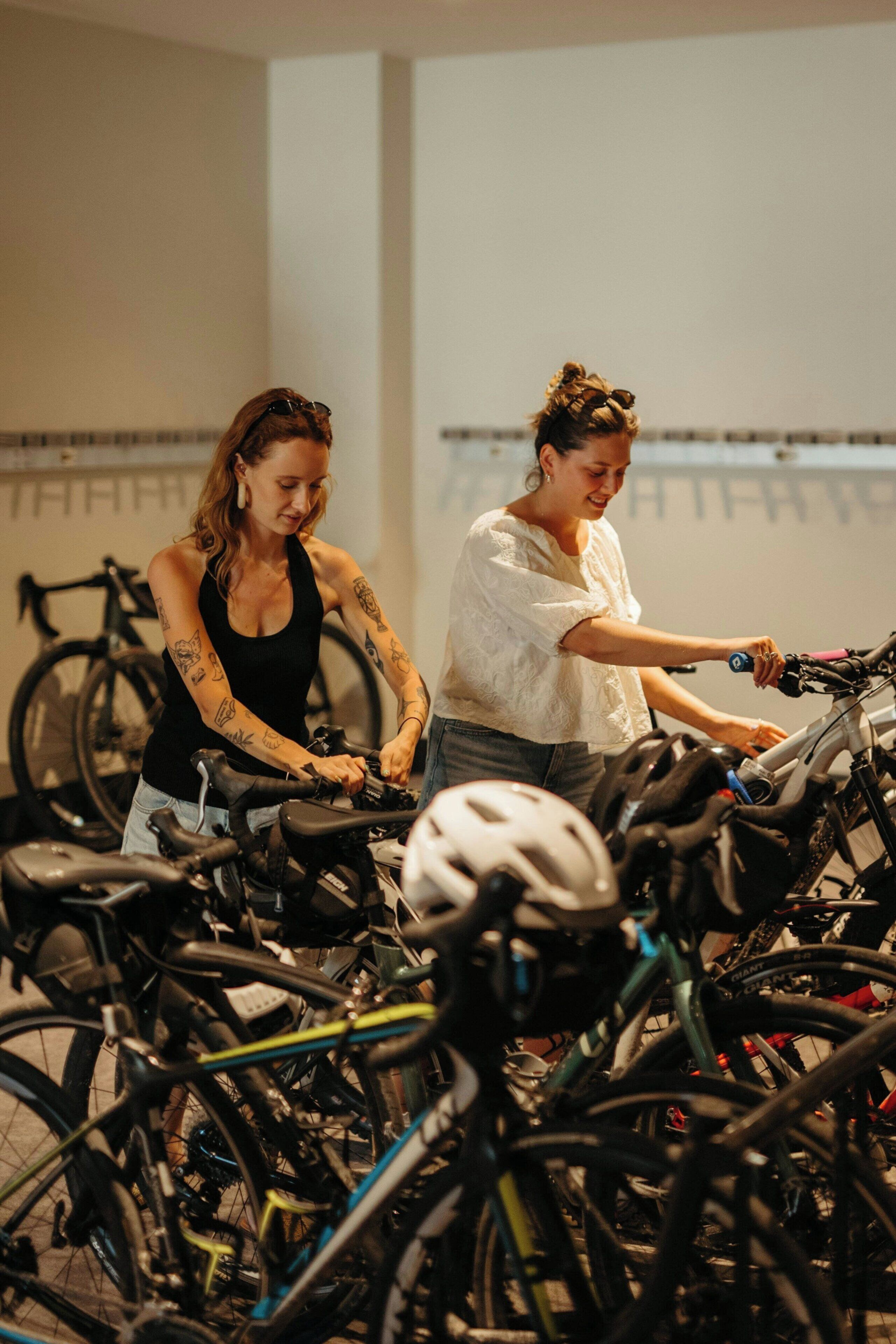 Two individuals on stationary bikes in a room with bicycles.