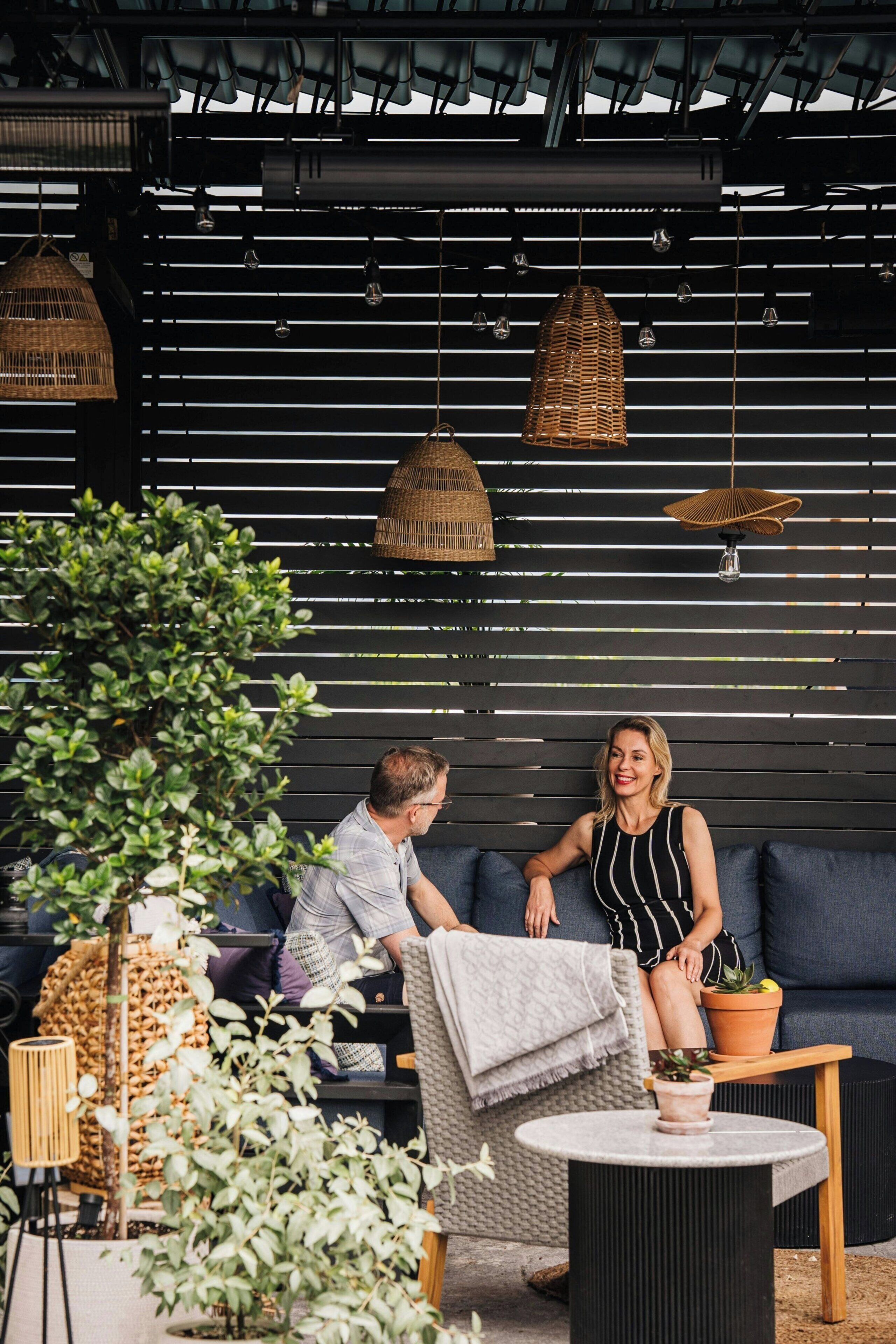 An outdoor seating area with a black backdrop, wicker hanging lamps, and potted plants.
