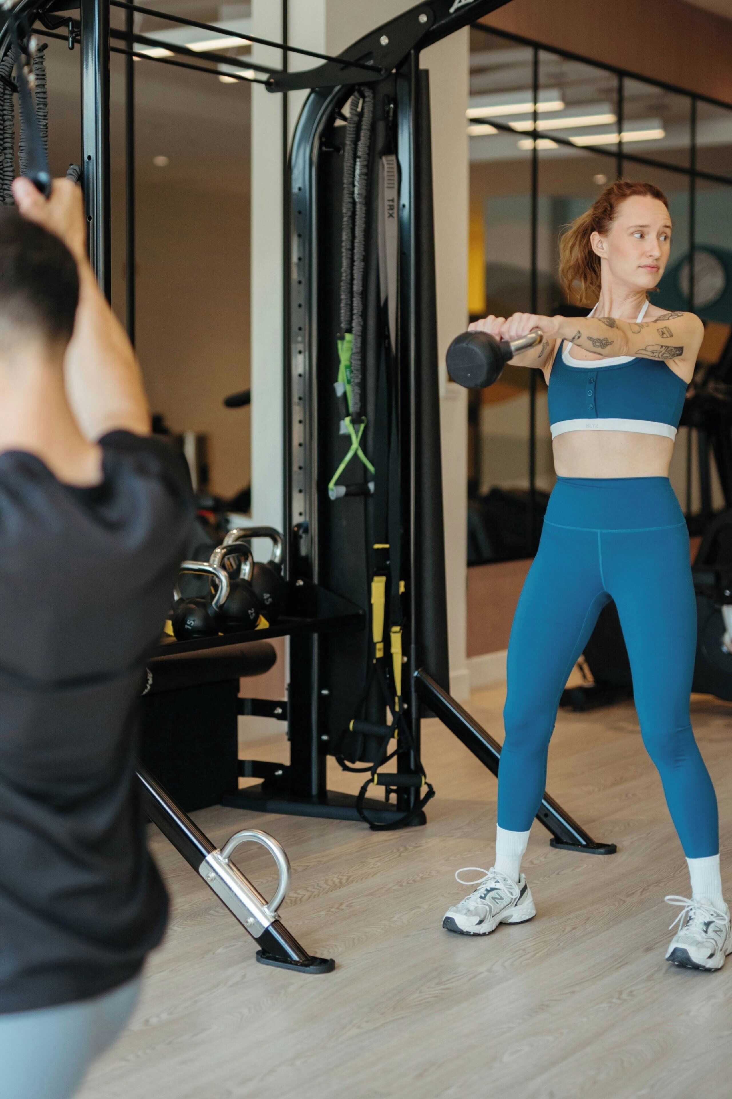 Un gimnasio con equipo de ejercicio y una persona usando una máquina de poleas.