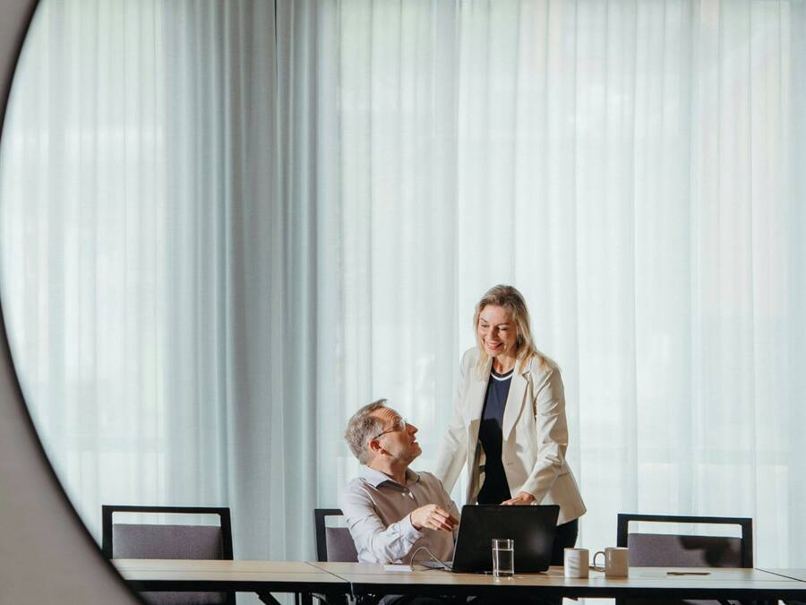 A conference room with a large table, chairs, a laptop, and a glass of water.