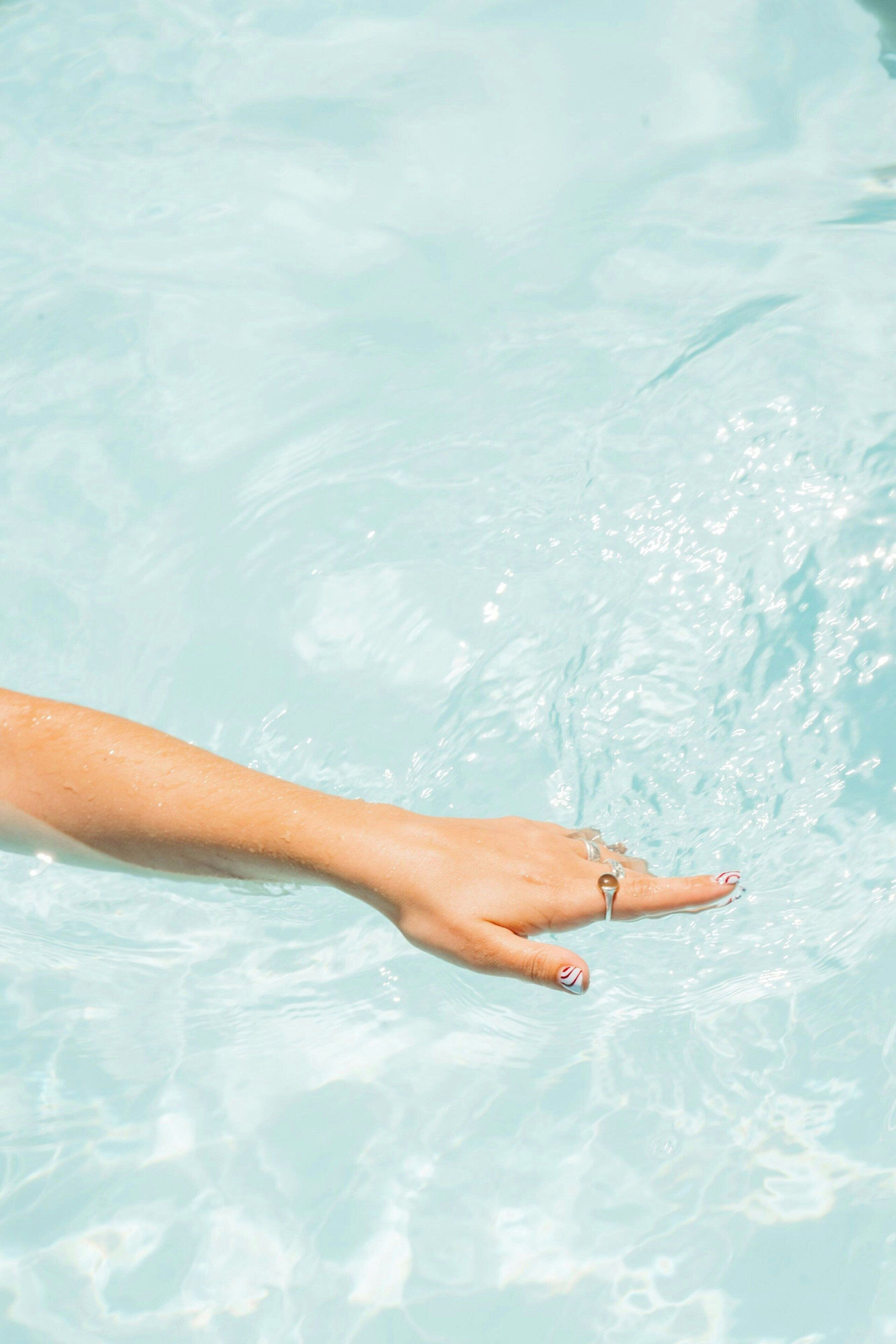 A hand reaching into clear blue water.