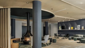A modern lobby with a central fireplace, seating areas, and a wall with framed pictures. - Residence Inn By Marriott Bromont (Bromont)