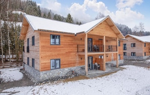 A wooden chalet with a balcony, stone foundation, and a snowy landscape.