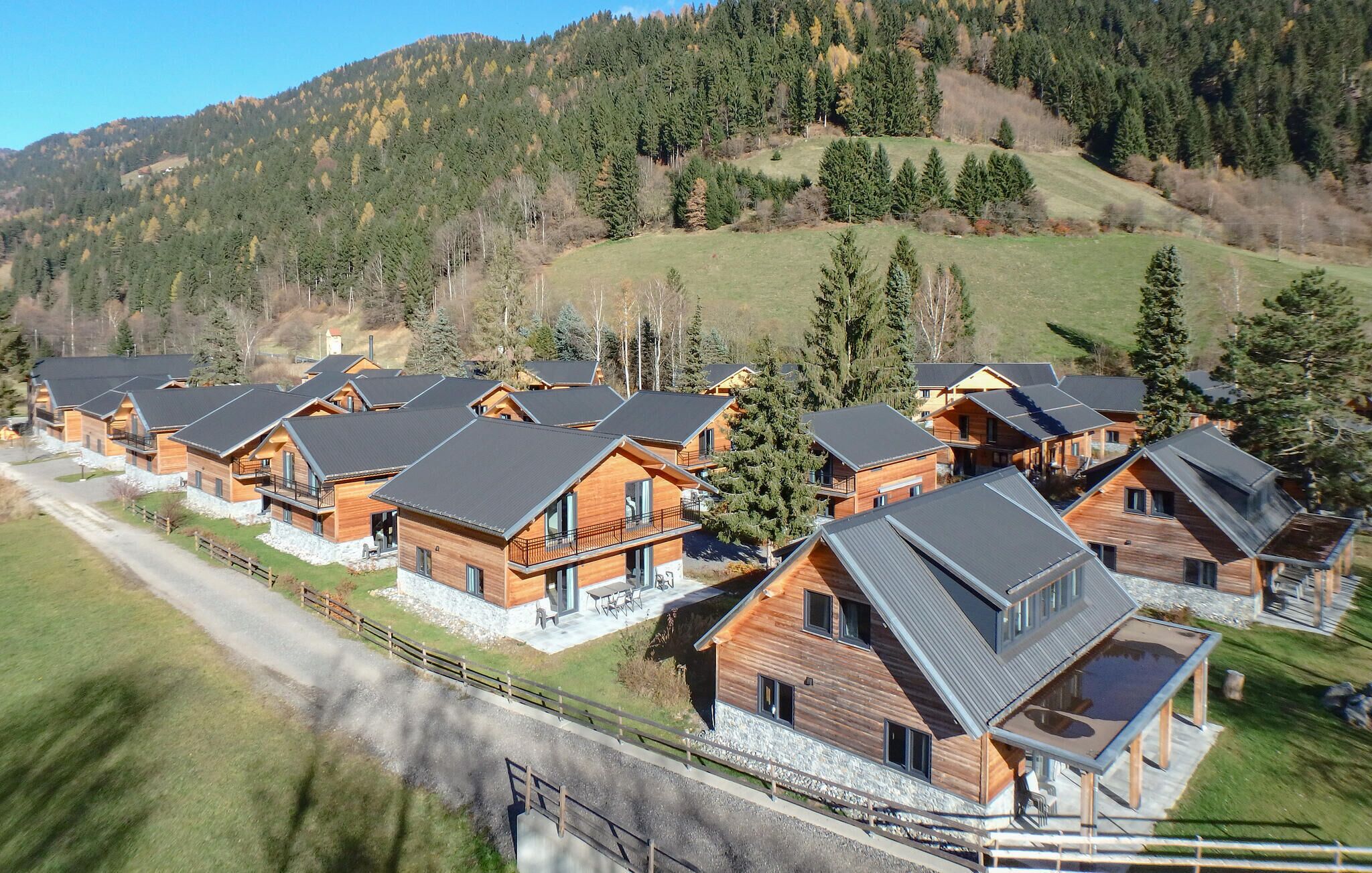 A row of wooden cabins with sloped roofs, set in a mountainous area with a clear sky.