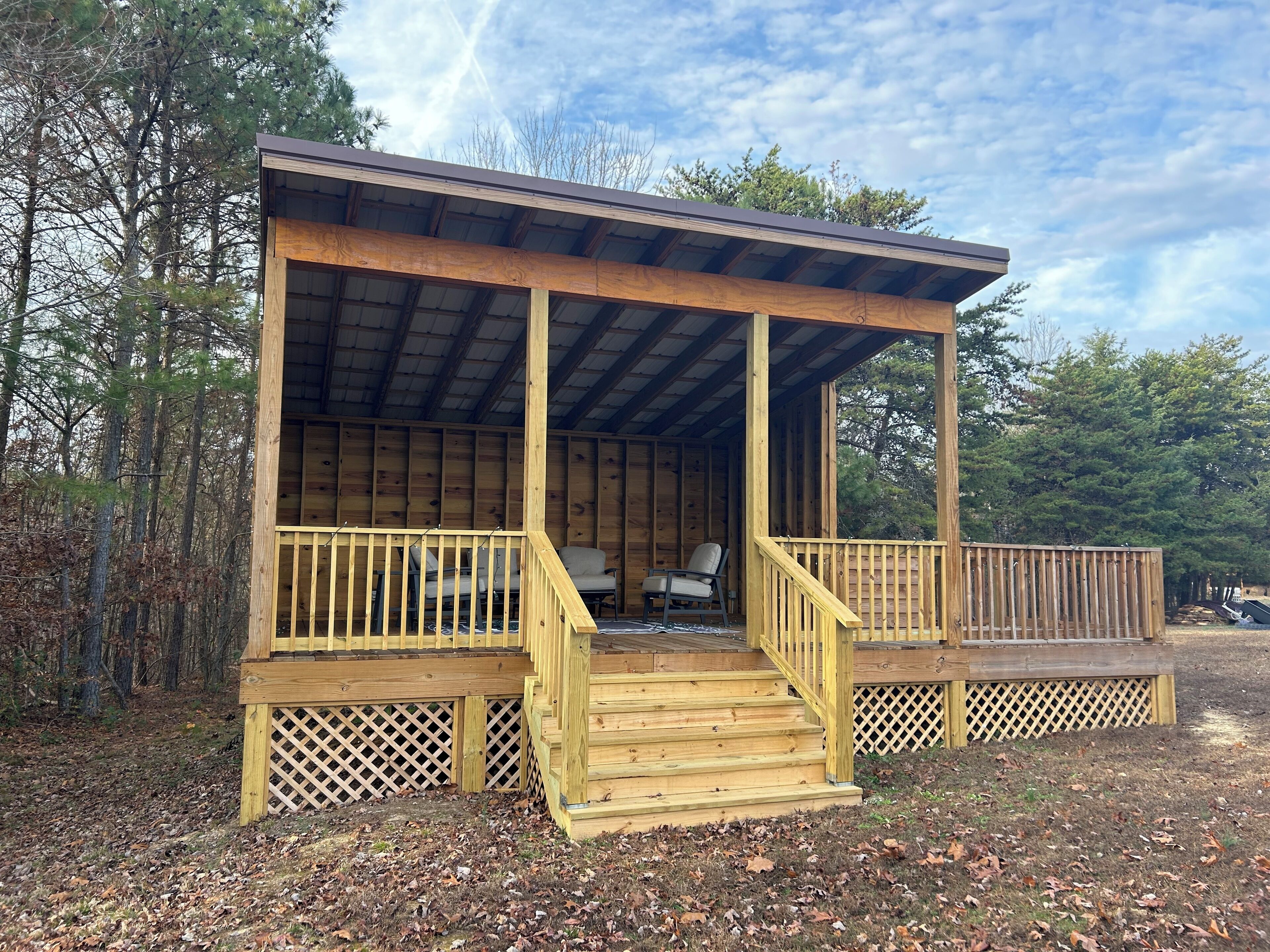 A wooden cabin with a covered porch, a staircase, and a view of the surrounding forest.