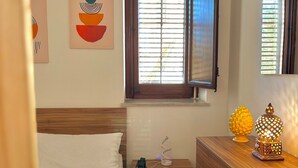 A hotel room with a bed, a bedside table with a lamp, a window with blinds, and artwork on the wall. - Charming apartment with terrace in the heart of the Sicilian capital (Palermo)