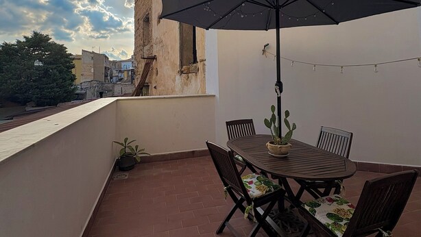 A balcony with a table and chairs, a potted plant, and a black umbrella. - Charming apartment with terrace in the heart of the Sicilian capital (Palermo)