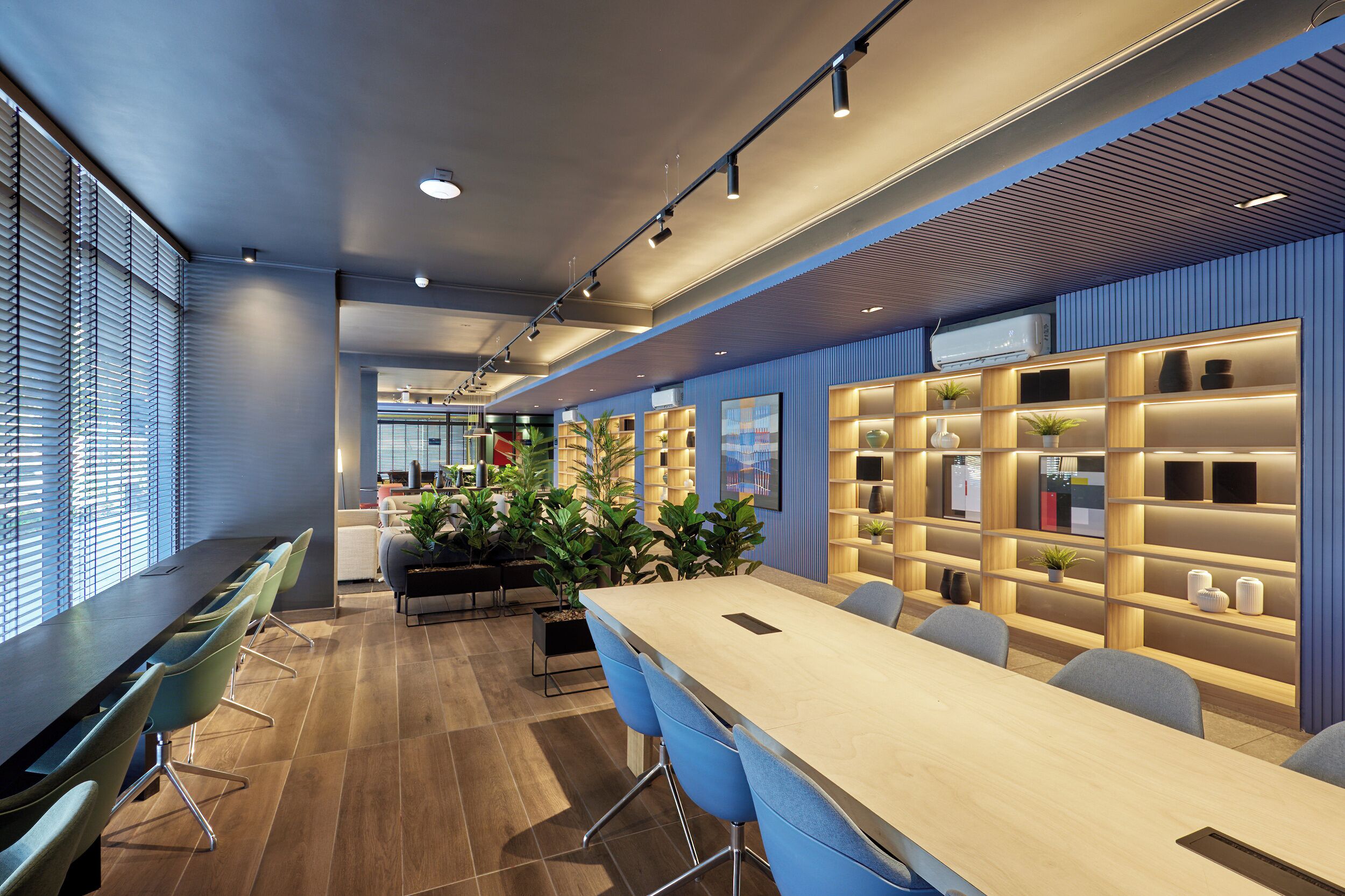 A modern meeting room with a long table, blue chairs, and shelves with decorative items.